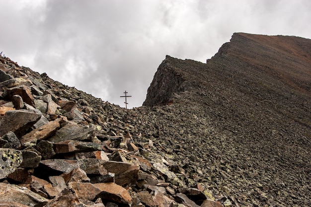 Mountain pass with an Orthodox cross on a background of clouds The stone slopes of the mountain Dangerous ascent to the mountain by crumbling stones Horizontal