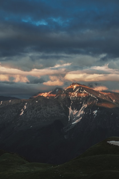 Mountain peak sunset landscape with gloomy dramatic mainly cloudy sky and orange and red sun beams