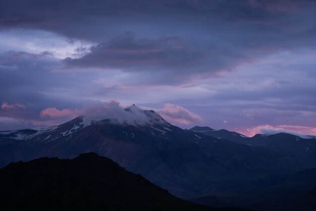 Mountain peak with snow and clouds during dramatic and colorful sunset.