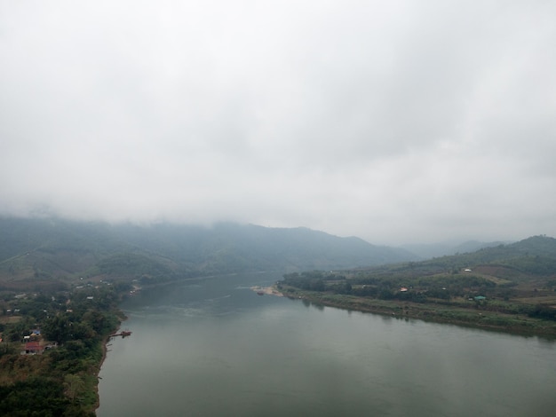 The mountain range is covered by clouds near the large river after the rain