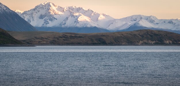 ニュージーランドのテカポ湖で撮影された前景の湖と日の出の間の山脈