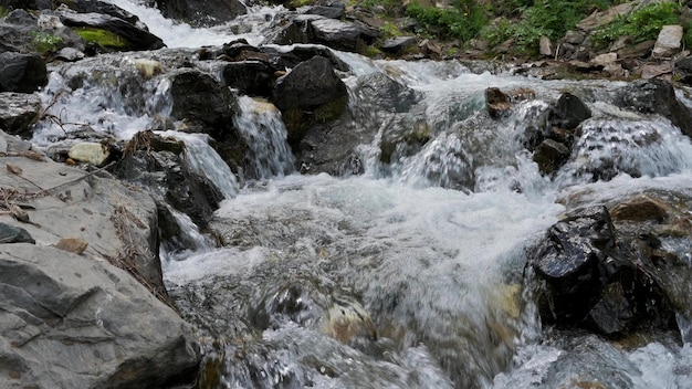Горный ручей с чистой водой и быстрым течением с камнями летом