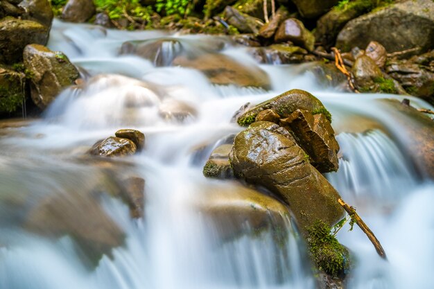 Mountain river with small waterfall with clear turquoise water falling down between wet boulders with thick white foam.