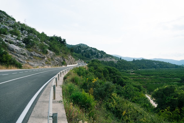 Mountain serpentine road with a fence near the cliff and views of the green hills and mountains