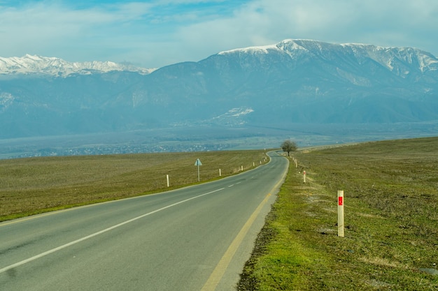 Mountain village with snowy peaks in the background long asphalt road in foreground