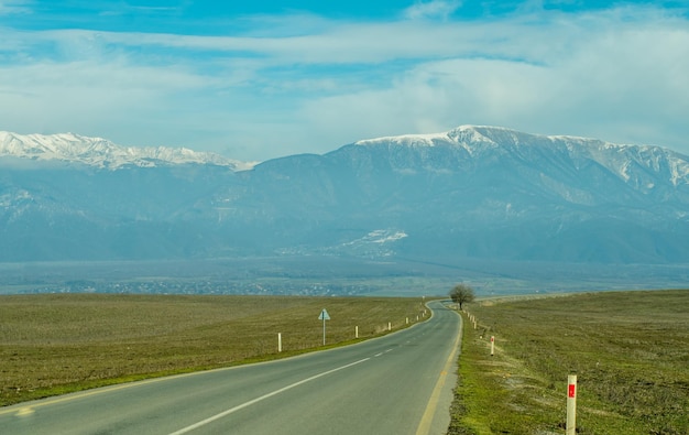 전경의 긴 아스팔트 도로를 배경으로 눈 덮인 봉우리가 있는 산악 마을