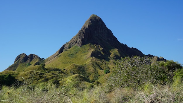 A mountain with a green field and a blue sky