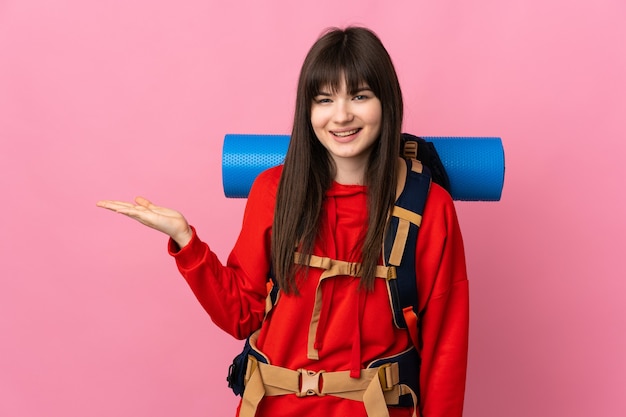 Mountaineer girl with a big backpack isolated on pink