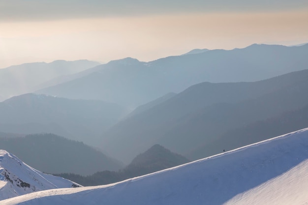 雪をかぶった山々と西の夕方の空とのライン上の登山家