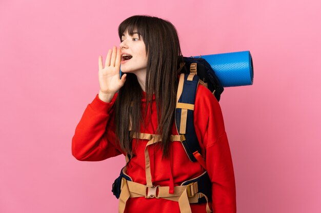 Mountaineer Ukrainian girl with a big backpack isolated on pink background shouting with mouth wide open