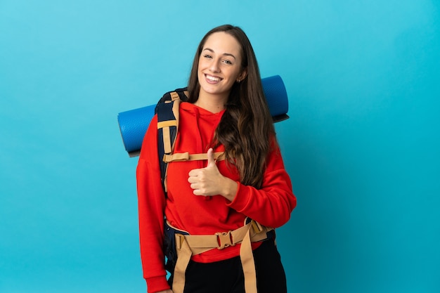 Mountaineer woman with a big backpack over isolated background giving a thumbs up gesture