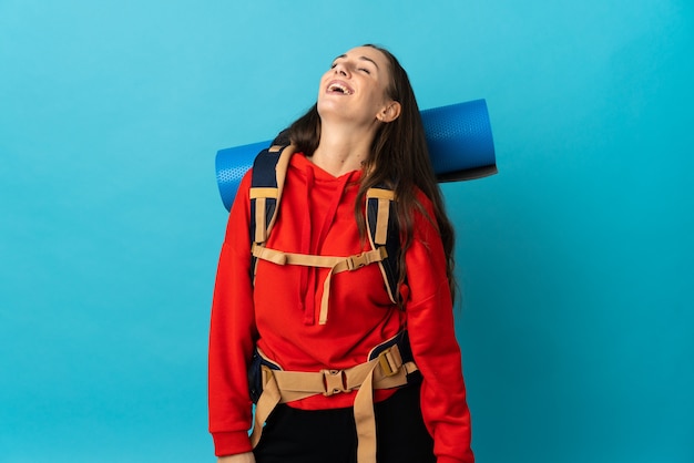 Mountaineer woman with a big backpack over isolated background laughing