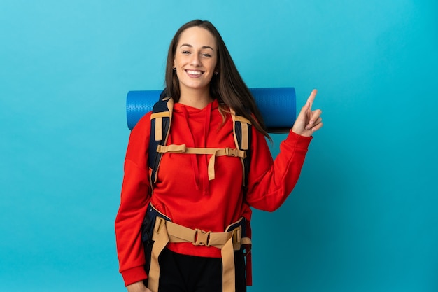 Женщина-альпинист с большим рюкзаком на изолированном фоне показывает и поднимает палец в знак лучших