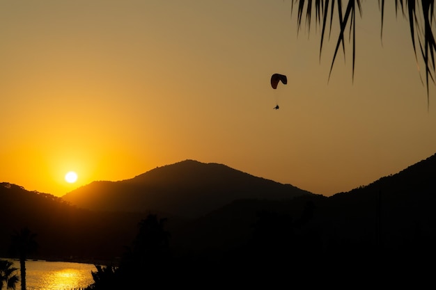 Mountainous landscape at sunset with the reflection of the sun on the sea and the silhouette of a paraglider flying in the sky