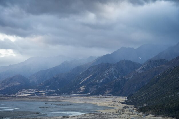 Mountains in alpine valley shrouded in thick dark clouds of approaching storm new zealand