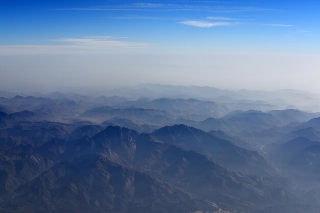 Горы и голубое небо с высоты птичьего полета из окна самолета впечатляющий пейзажный фон