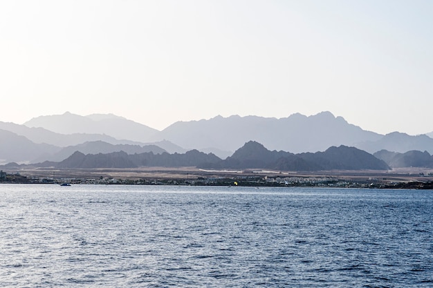 Mountains in the fog on the beach. View from the water. Summer landscape with sea and mountain range