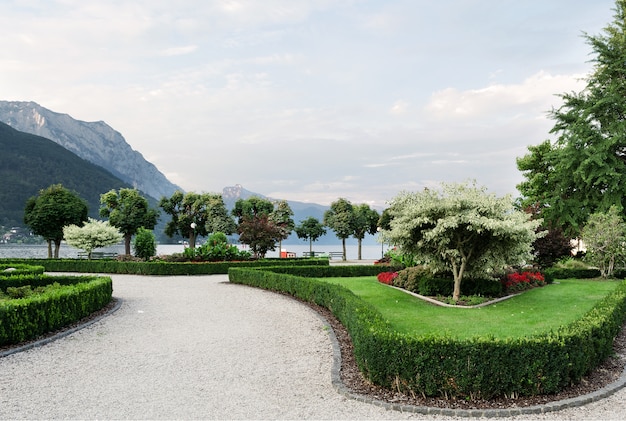 the mountains, the lake and the embankment of the city with trimmed trees, shrubs, lawn and flower beds.