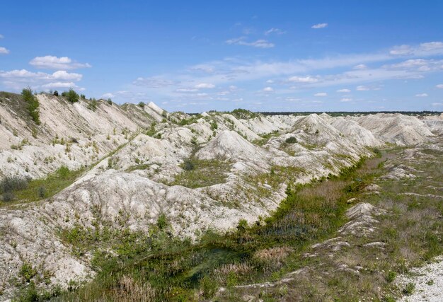 Mountains of processed chalk ore overgrown with green young plants on the background of special equipment