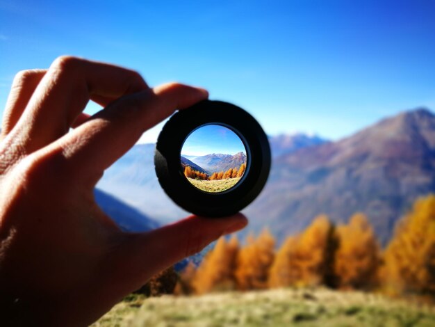 写真 人によって保持されているレンズを通して見られる山々