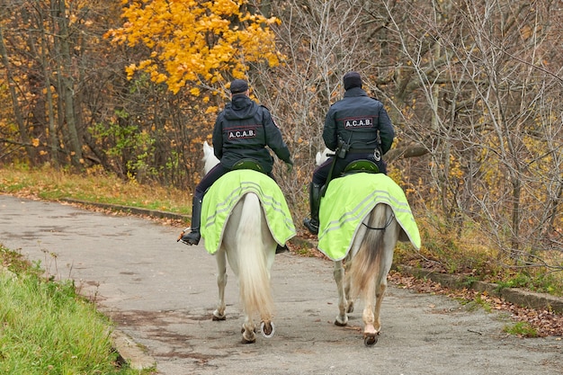 Mounted police in autumn city park, back view. All Cops Are Bastards acronym, anarchism movement concept. Two police officers on horseback patrol the park.