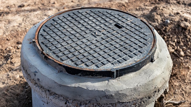 Mounting of a heavy cast-iron sewer hatch on a concrete well. Close-up. Modern sewerage and water supply in the city.