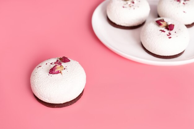 Mousse dessert covered with white chocolate and decorated with rose buds on pastel pink background