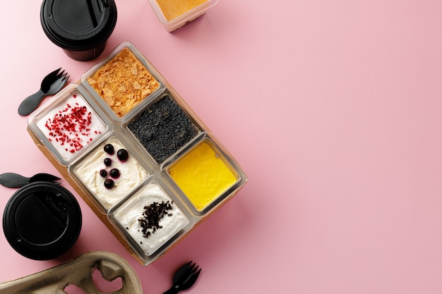 Mousse desserts in square plastic boxes with different toppings on pink table