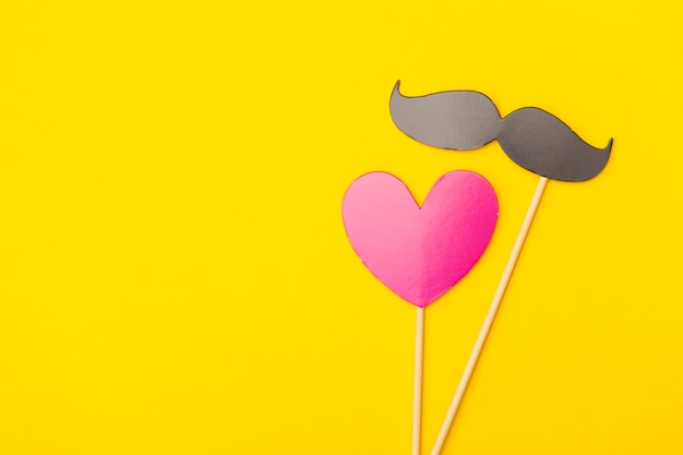 Moustache and heart on a stick on a bright yellow background