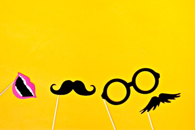 Photo moustache, tie, glasses, red mouth on wooden sticks against bright yellow background flat