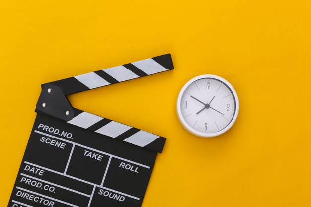 Photo movie clapper board and clock on yellow background. filmmaking, movie production, entertainment industry. top view