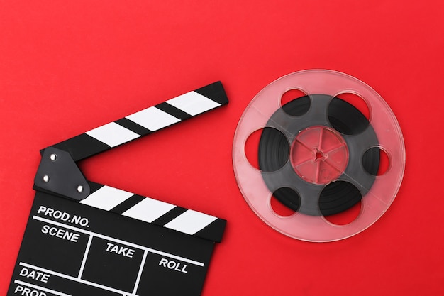 Movie clapper board and film reel on red background. Cinema industry, entertainment. Top view