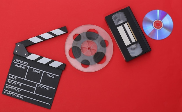 映画のカチンコとフィルムリール、赤い背景のビデオカセット。映画産業、エンターテインメント。上面図