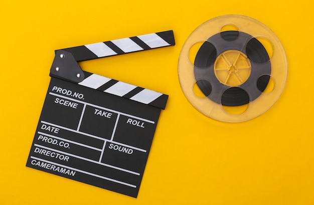 Movie clapper board and film reel on  yellow background. Cinema industry, entertainment. Top view