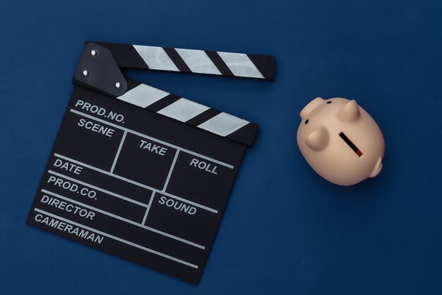 Movie clapper board and piggy bank on classic blue background. Filmmaking, Movie budget, Entertainment industry. Color 2020. Top view