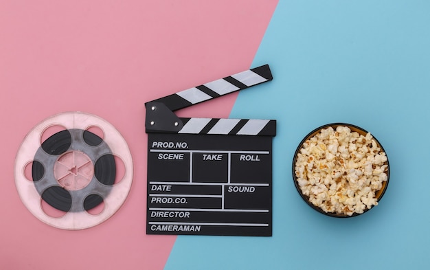 Movie clapper board, popcorn bowl and film reel on pink blue background. Entertainment industry. Top view. Flat lay