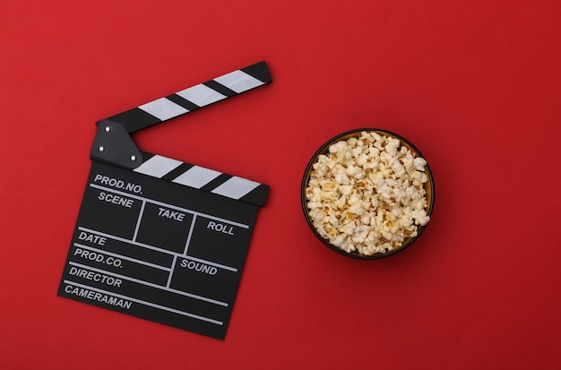 Movie clapper board, popcorn bowl on red background. Entertainment industry. Top view. Flat lay