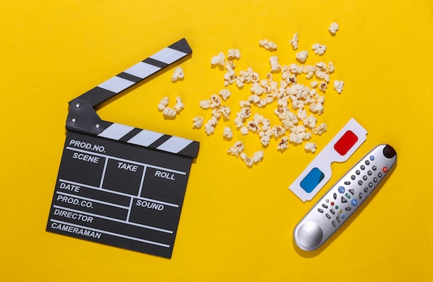 Movie clapper board, popcorn, tv remote and 3d glasses on yellow background with deep shadows. Entertainment industry. Top view