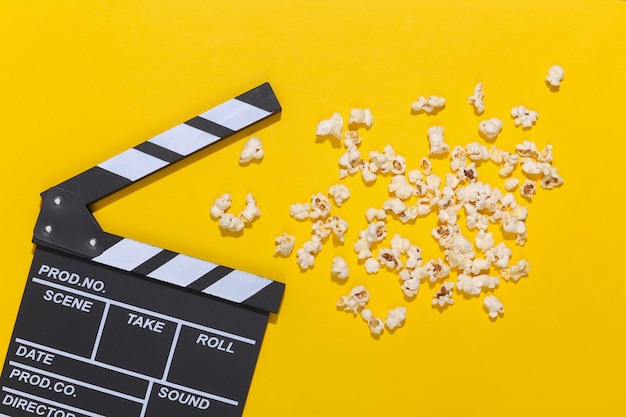 Movie clapper board, popcorn on yellow background with deep shadows. Entertainment industry. Top view