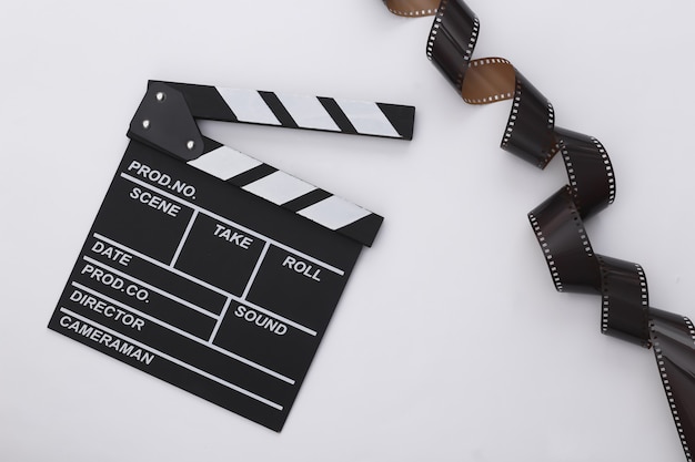 Movie clapper board with film tape on white background. Filmmaking, Movie production, Entertainment industry. Top view