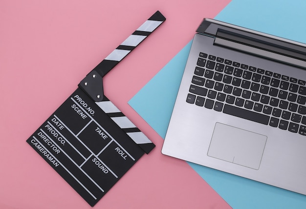 Доска с хлопушкой фильма с ноутбуком на сине-розовом пастельном фоне. Кинопроизводство, Кинопроизводство, Индустрия развлечений. Вид сверху