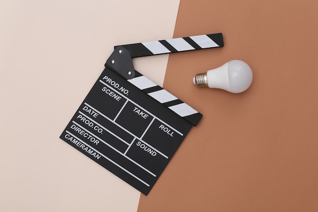 Movie clapper board with light bulb on beige brown background. Filmmaking, Movie production, Entertainment industry. Top view