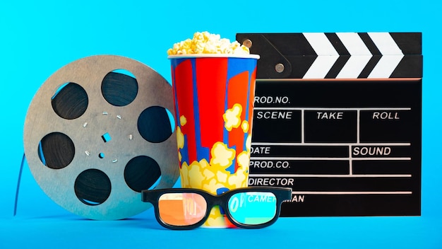 Movie clapper pop corn 3D glasses and film reel on blue background Collage design