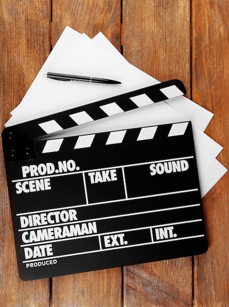 Movie clapper with sheets of paper and pen on wooden planks background