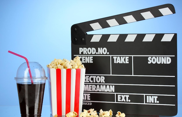 Movie clapperboard cola and popcorn on blue background