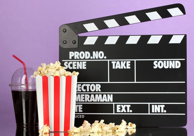 Movie clapperboard cola and popcorn on purple background