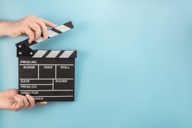 Movie clapperboard in hands on a blue space