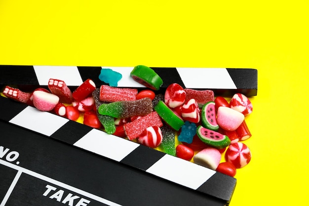 Movie clapperboard with assorted candy on a yellow background