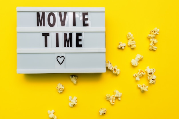 Movie Time text on a light box. Scattered salty popconn on yellow background