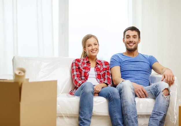 moving, home and couple concept - smiling couple relaxing on sofa in new home